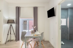 Een moderne kamer met een eettafel, stoelen, een driepoot lamp, een flatscreen televisie en uitzicht op buiten.