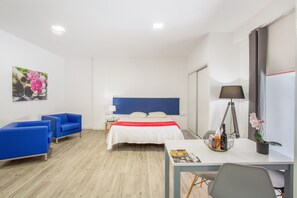 Een hotelkamer met een bed, een bureau, twee blauwe stoelen, een lamp en een schilderij aan de muur.