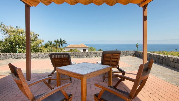 Un porche techado con una mesa y sillas, con vistas a la costa.