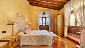 Un dormitorio con dos camas, suelo de madera, techo de madera, una ventana con cortinas y una mesita de noche con lámpara.
