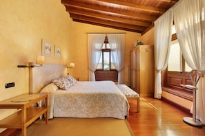 Un dormitorio con dos camas, suelo de madera, techo de madera, una ventana con cortinas y una mesita de noche con lámpara.