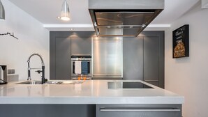 Et moderne køkken med en stor ø, rustfrie hvidevarer og en hængende lampe.