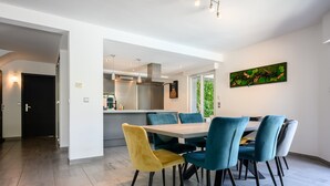 Et moderne spiseområde med et træbord og stole, et køkken i baggrunden og et billede på væggen.