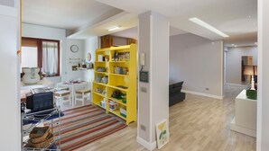 A modern living room with a yellow bookshelf, a dining area with a white table, and a kitchen area with a stove.