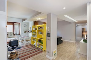 A modern living room with a yellow bookshelf, a dining area with a white table, and a kitchen area with a stove. - Room 'Casa Frank -  2' with Mountain View, Wi-Fi and Air Conditioning (Torre Annunziata)