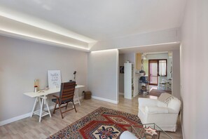 Een moderne woonkamer met een wit bureau, een kamerbreed tapijt, een witte bank en uitzicht op een andere kamer met een keuken.