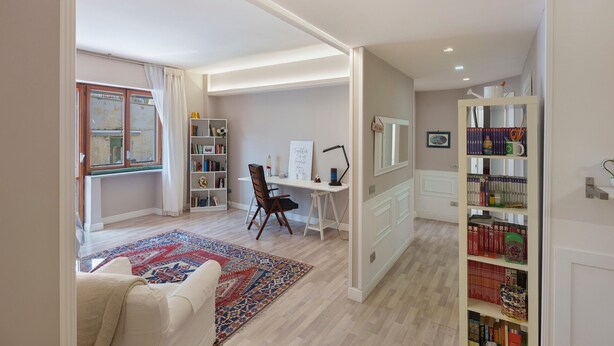 A modern living room with a large window, a desk, and a bookshelf.