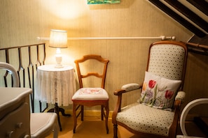 A room with a wooden chair, a table with a lace tablecloth, and a lamp.