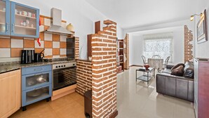 A modern kitchen with a brick accent wall, a dining area with a table and chairs, and a living room with a sofa.