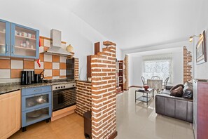 Une cuisine moderne avec un mur d’accent en briques, un coin repas avec une table et des chaises, et un salon avec un canapé.