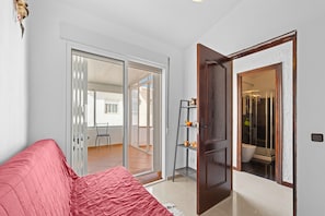 Ein Zimmer mit einer roten Couch, einer Holztür, einer Glastür, die auf einen Balkon führt, und einem kleinen Regal mit Dekoration.