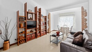 A living room with a sofa, coffee table, wooden bookshelves, a television, and a dining area with a table and chairs.