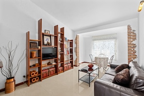 Ein Wohnzimmer mit einer Couch, einem Couchtisch, Holzregalen, einem Fernseher und einem Essbereich mit Tisch und Stühlen.