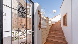 A white building with a black gate, a staircase, and a white fence.