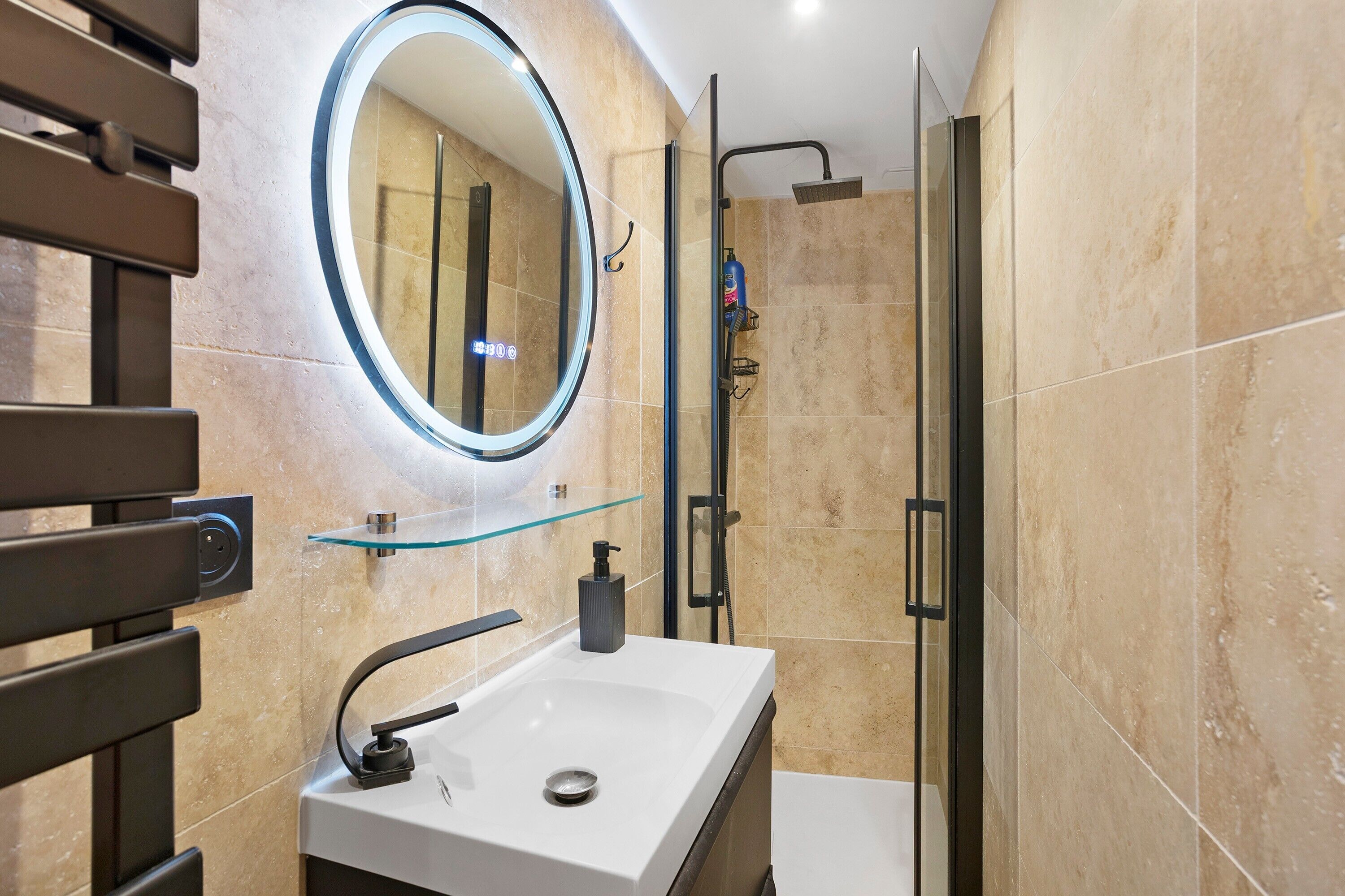 Un bagno moderno con uno specchio rotondo, un lavandino bianco, una mensola in vetro e uno spazio doccia.