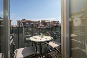 Ein Balkon mit einem runden Tisch und zwei gepolsterten Stühlen, mit Blick auf eine Stadtlandschaft und Gebäude.