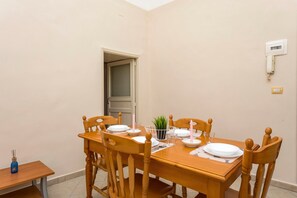 Un coin repas avec une table en bois dressée pour quatre personnes, des chaises, une petite table d’appoint et une porte donnant sur une autre pièce.