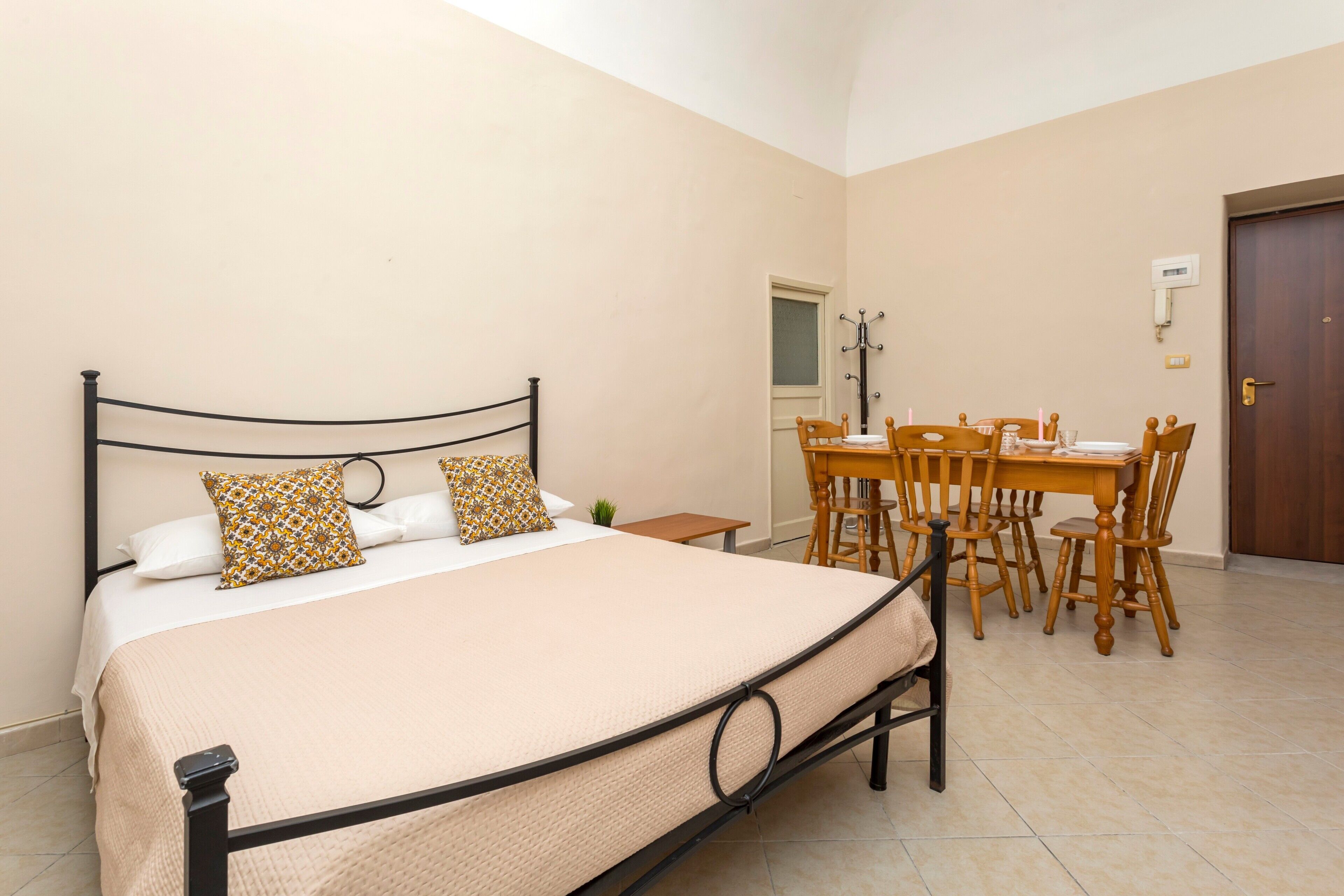 A bedroom with a bed, a dining table, chairs, a small table, and a door.