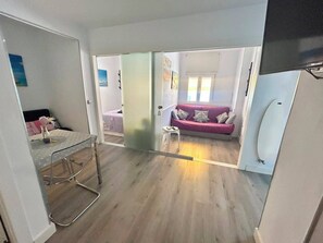 A compact room with a bed, a pink sofa, and a small table. - Oasis Sitges Apartment: Relaxing, Centrally Located, and With a Community Pool (Sitges)