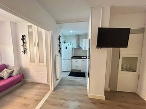 A modern apartment with a living room, kitchenette, and a TV mounted on the wall. - Oasis Sitges Apartment: Relaxing, Centrally Located, and With a Community Pool (Sitges)