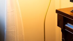 Una habitació amb una làmpada de peu, un armari de fusta i una cortina.