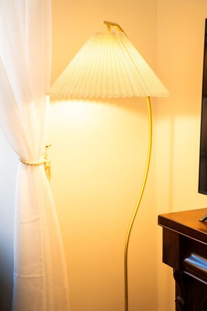 Ein Zimmer mit einer stehenden Stehlampe, einem Holzschrank und einem Vorhang.
