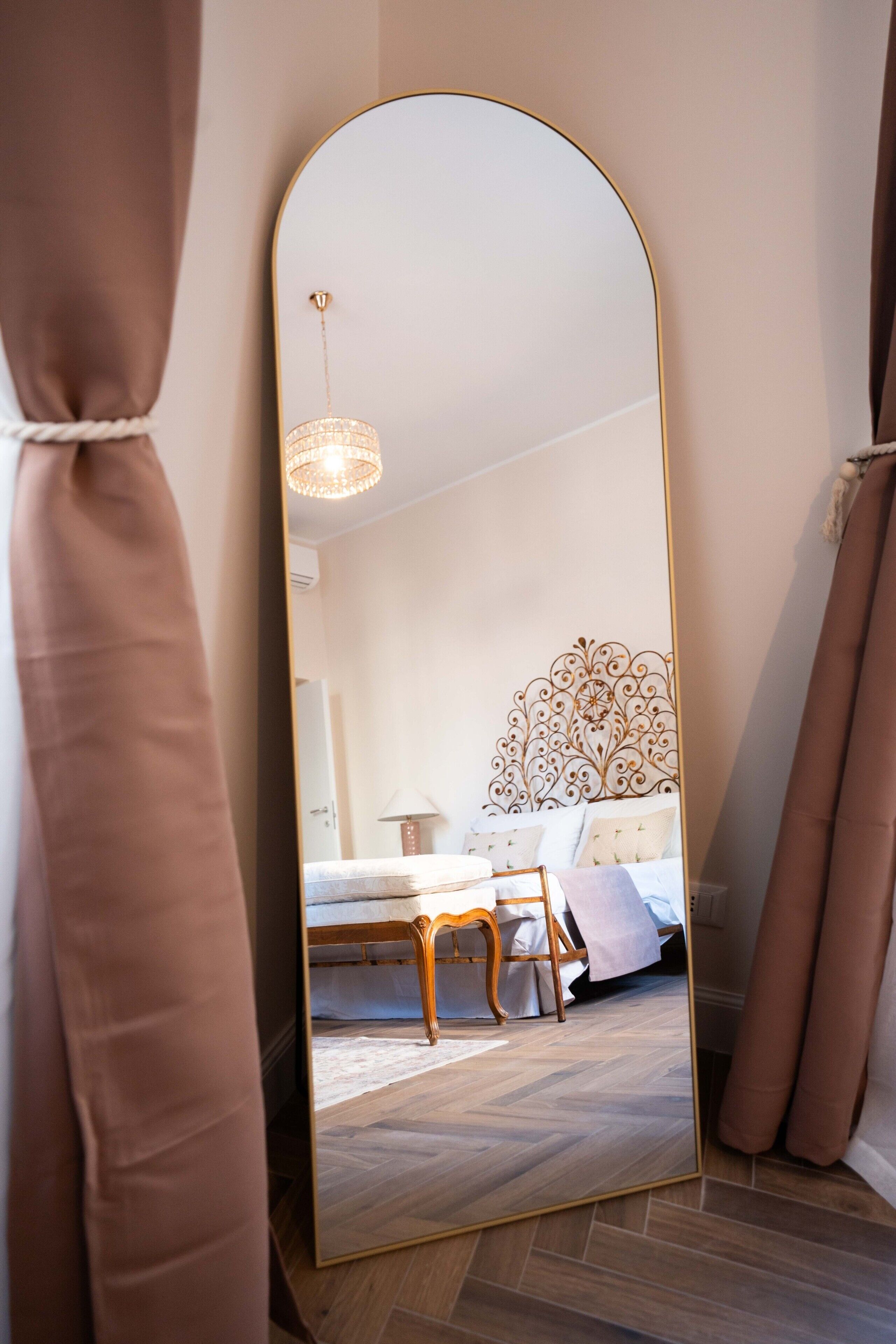 A bedroom with a large mirror, a bed with a decorative headboard, a bedside table, and a hanging light fixture.