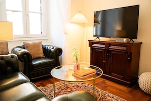 Un salon avec un canapé en cuir, une table basse en verre, un téléviseur à écran plat posé sur un meuble en bois et un tapis à motifs.
