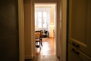 Ein Flur, der in einen Essbereich mit Tisch und Stühlen, einer Lampe und einem fenster mit Vorhängen führt.