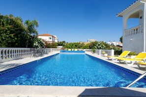 A rectangular swimming pool with clear blue water, surrounded by a white balustrade and yellow lounge chairs.