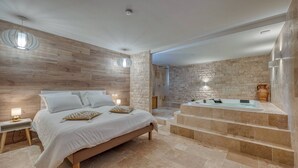 A bedroom with a large bed, a built-in bathtub, and a stone wall. - Luxurious Romantic Suite with Jacuzzi, Wi-Fi, and Air Conditioning (Saint-Martin-d'Hères)