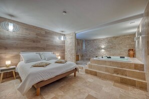 Un dormitorio con una cama grande, una bañera integrada y una pared de piedra.