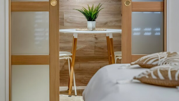 A room with a bed, a wooden wardrobe with frosted glass panels, a small table with a plant, and a wall-mounted light. - Luxurious Romantic Suite with Jacuzzi, Wi-Fi, and Air Conditioning (Saint-Martin-d'Hères)
