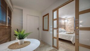 A bedroom with a bed, a bedside table with a plant, a mirror, and a door leading to another room. - Luxurious Romantic Suite with Jacuzzi, Wi-Fi, and Air Conditioning (Saint-Martin-d'Hères)