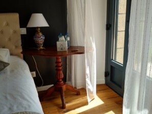 Un dormitorio con una cama, una mesita de noche con lámpara, una ventana con cortinas y una puerta.