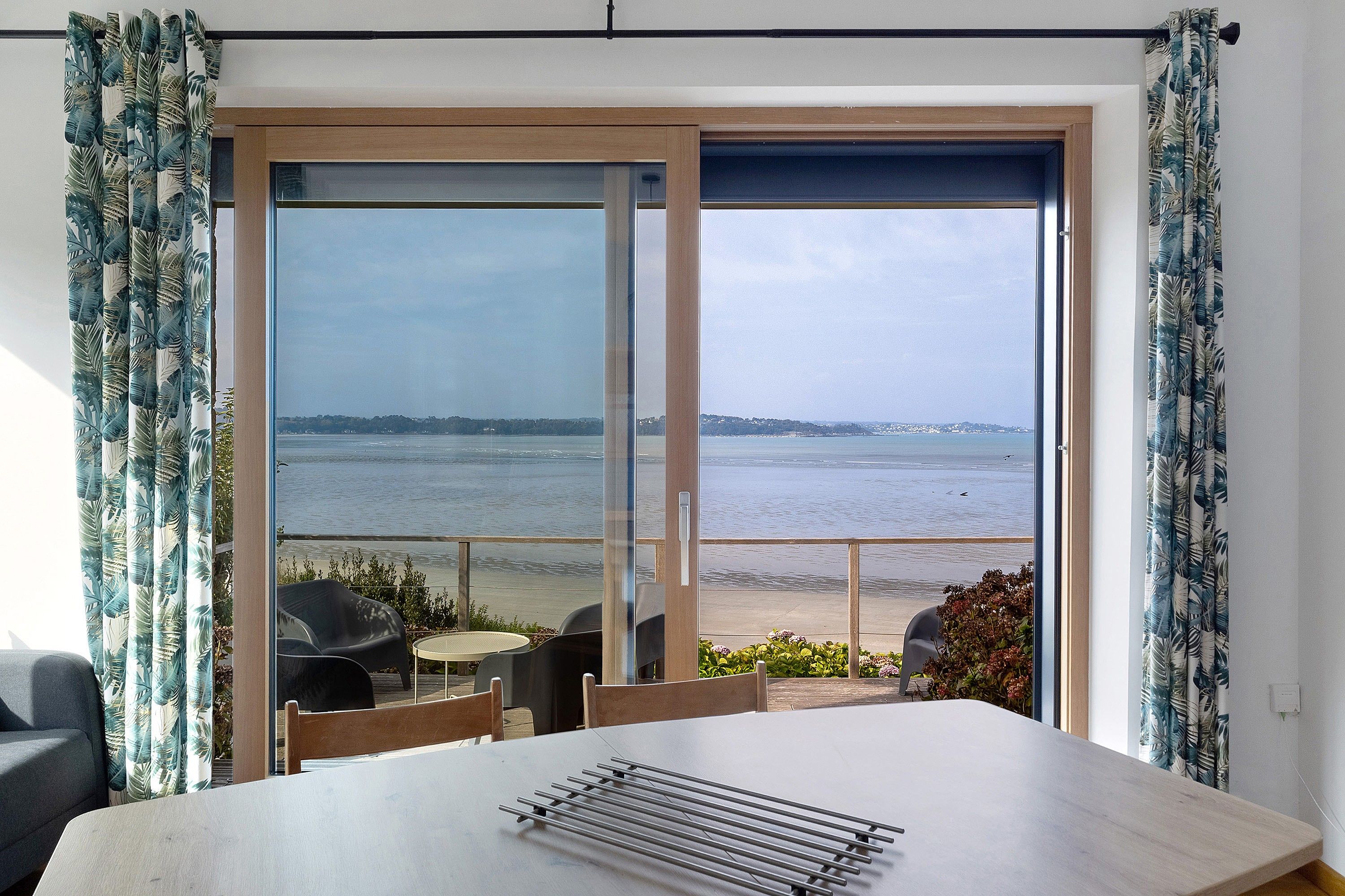 A room with a view of the beach, a table, and chairs.
