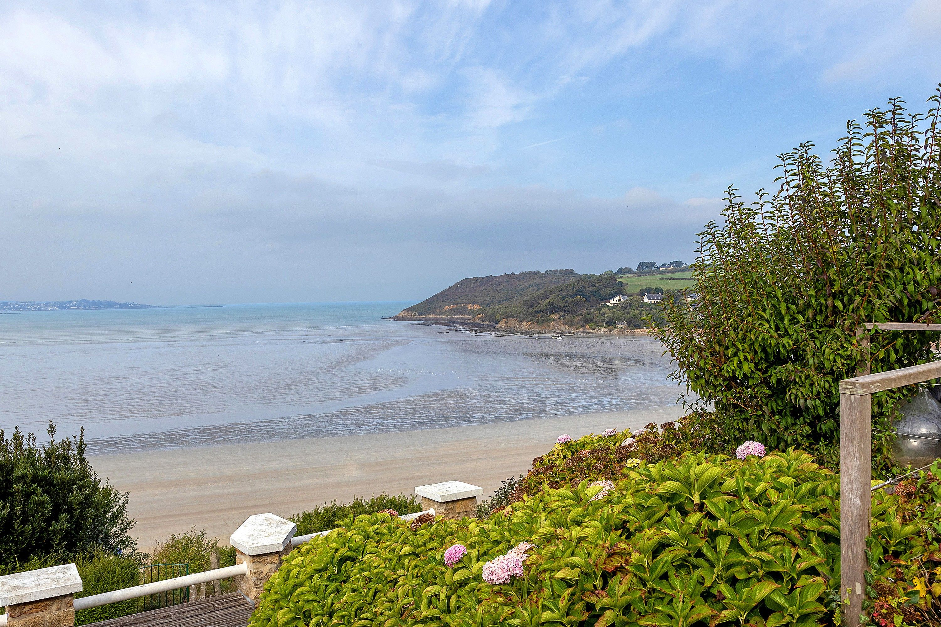 A coastal landscape with a beach, greenery, and a distant view of houses.