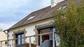 Une maison à deux étages, avec un toit en pente, une façade en pierre et une cheminée bien visible.