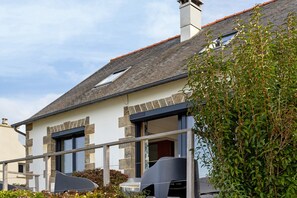 Une maison à deux étages, avec un toit en pente, une façade en pierre et une cheminée bien visible.