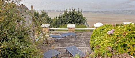 A wooden deck with two lounge chairs and a stone bench overlooking a beach.