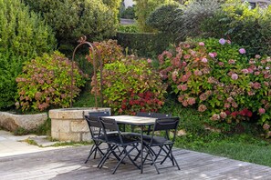 Un espace extérieur aménagé avec une table et des chaises, entouré d’une végétation luxuriante et de plantes en fleurs.