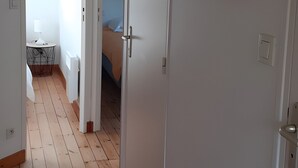 Un pasillo con suelo de madera, una puerta blanca y un cuadro enmarcado en la pared.