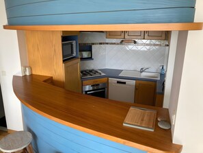 Una cocina compacta con encimera de madera, microondas, cocina a gas, lavavajillas y fregadero.