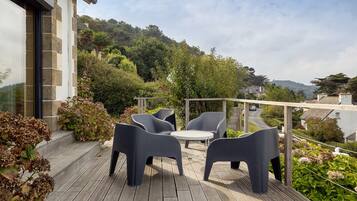An outdoor patio with modern furniture, surrounded by lush greenery and a view of a hillside.