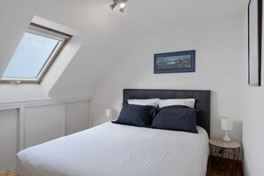 A bedroom with a bed, a nightstand, a lamp, a framed picture, and a skylight. - Holiday Home 'Maison Ty Bastian, 100 M²' with Sea View, Private Terrace and Wi-Fi (Saint-Michel-en-Grève)
