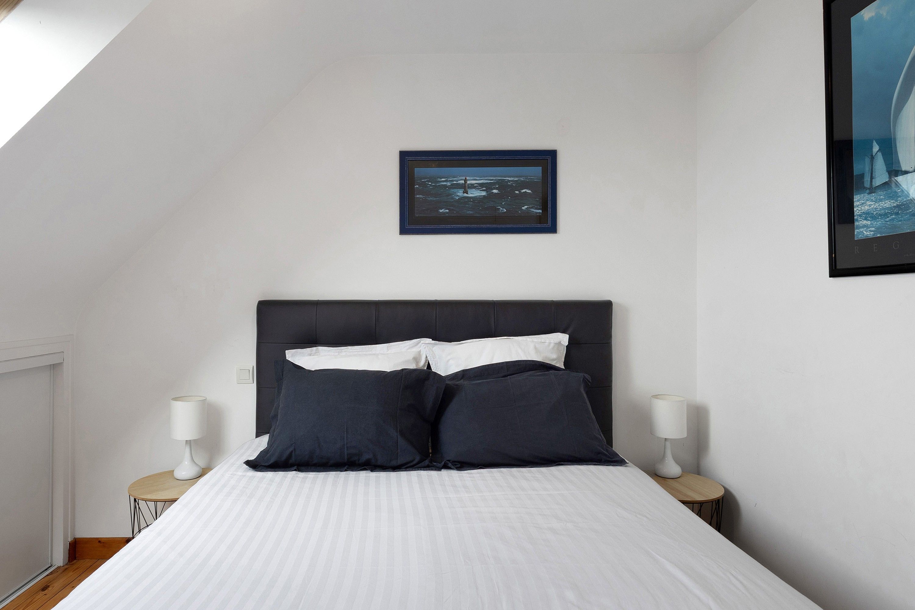 A bedroom with a bed, two bedside tables, a nightstand, a framed picture on the wall, and a window.