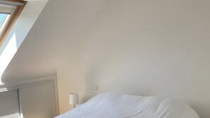 Un dormitorio con cama, piso de madera, lámpara en el techo y ventana.