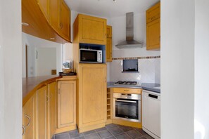 A compact kitchen with wooden cabinets, a microwave, a stove, and a dishwasher. - Holiday Home 'Maison Ty Bastian, 100 M²' with Sea View, Private Terrace and Wi-Fi (Saint-Michel-en-Grève)