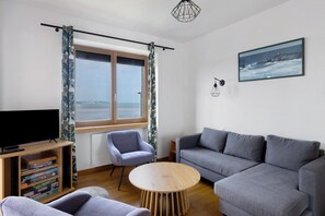 A living room with a sofa, armchair, and a round wooden table. - Holiday Home 'Maison Ty Bastian, 100 M²' with Sea View, Private Terrace and Wi-Fi (Saint-Michel-en-Grève)