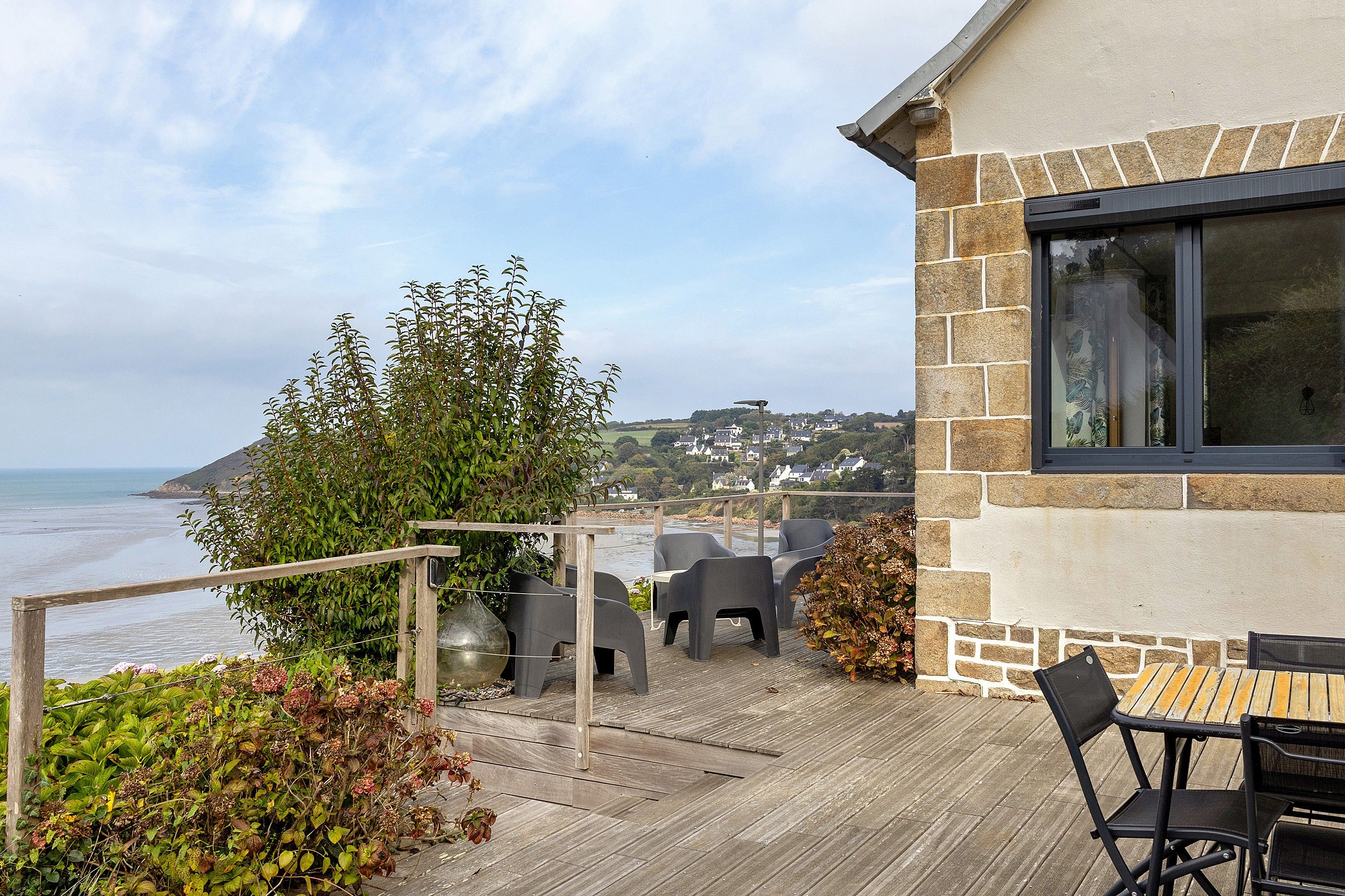 Eine Holzterrasse mit Sitzgelegenheit mit Blick auf eine Küstenlandschaft.